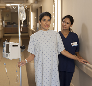 Patient walking in hospital hall with an I.V. pole and nurse.