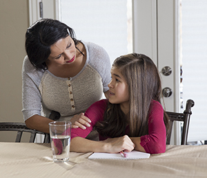 Girl sitting with paper and pen, talking to woman.